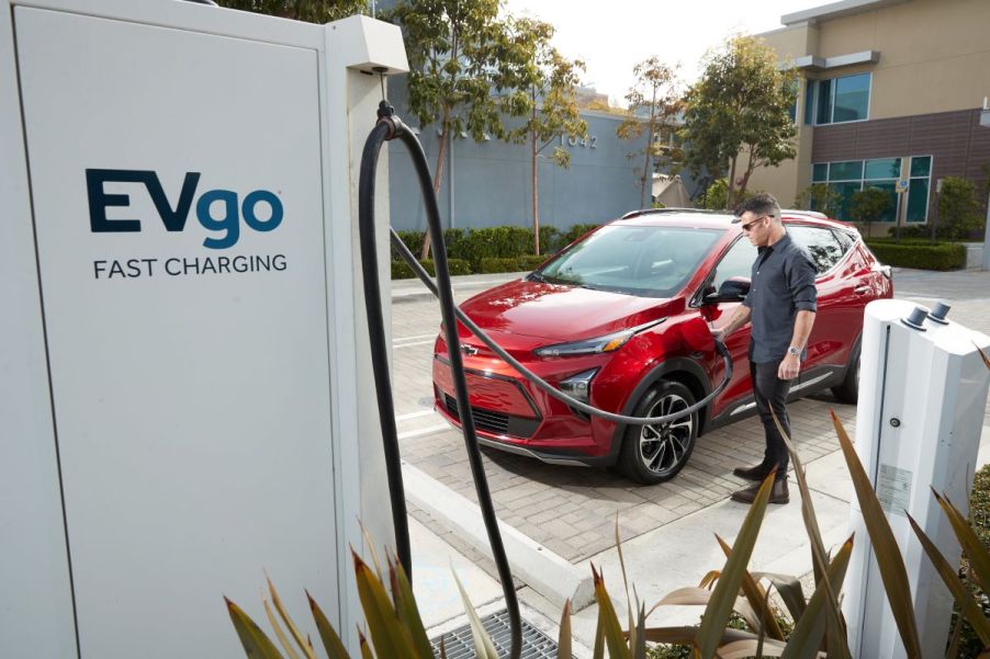 A red 2022 Chevy Bolt EUV electric compact SUV plugged into an EVgo fast charging station