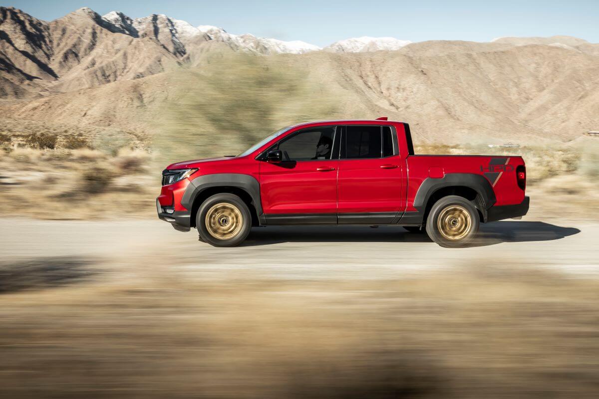 A side profile shot of a red 2023 Honda Ridgeline Sport with HPD Package midsize pickup truck on a desert road