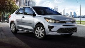 A silver-gray 2023 Kia Rio subcompact sedan model parked in a big city near a river walkway