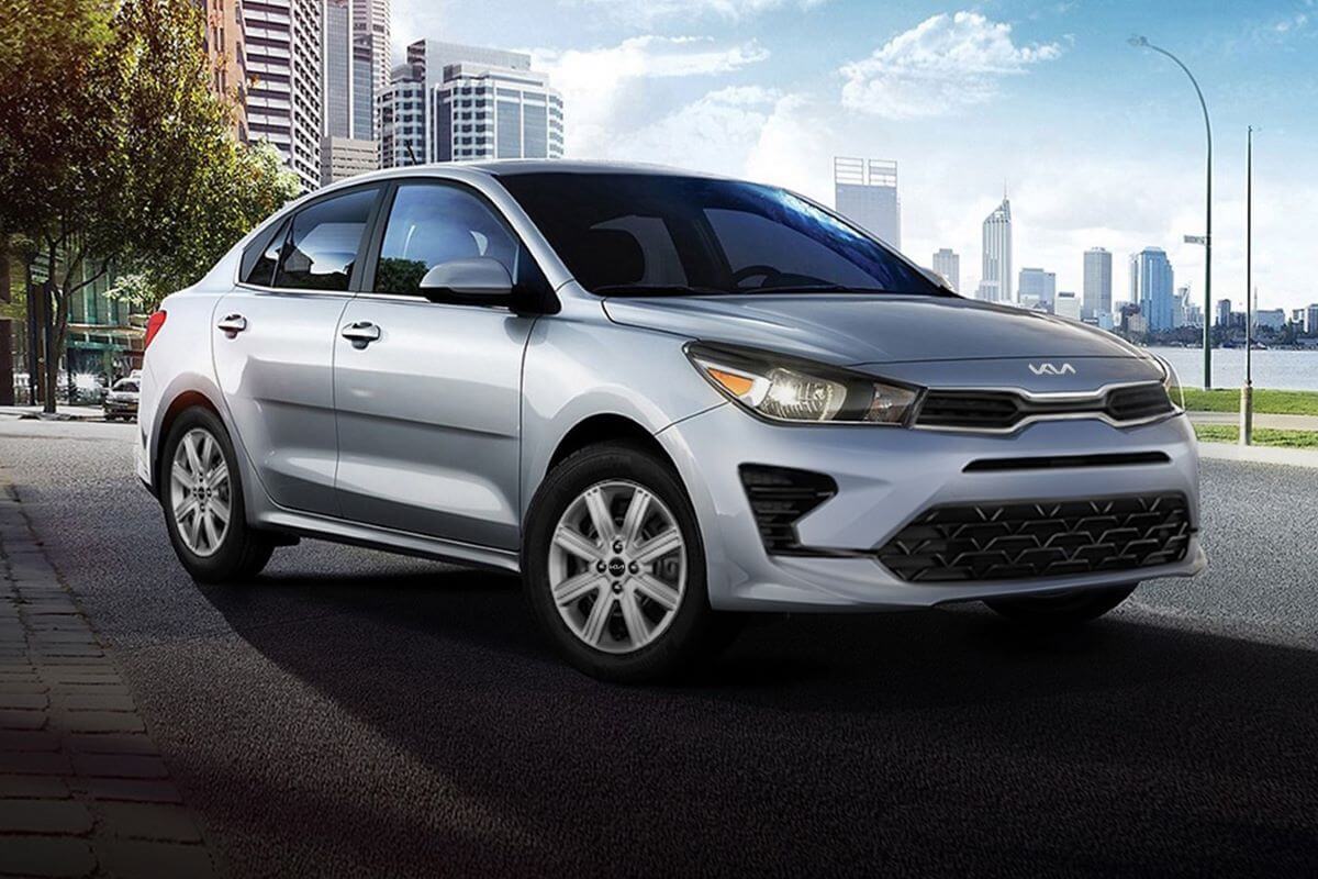 A silver-gray 2023 Kia Rio subcompact sedan model parked in a big city near a river walkway