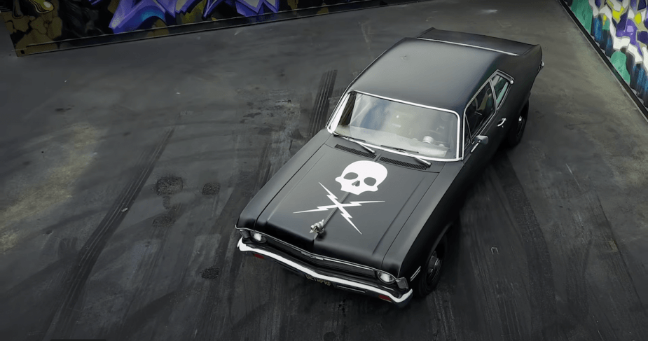 Bird's-eye view of a 1970 Chevrolet Nova parked in a paved lot, colorful painted walls visible in the background.