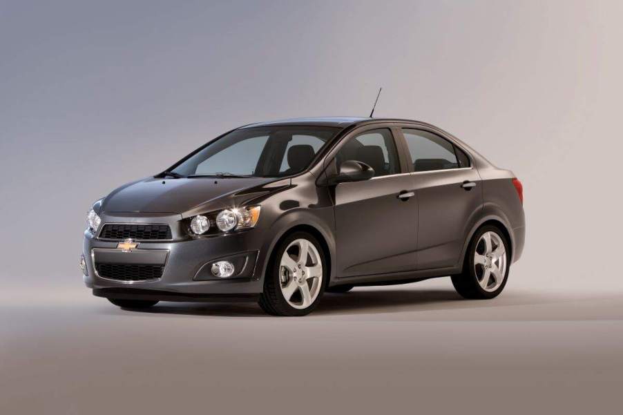 A grey 2015 Chevy Sonic parked in a blue and grey room.