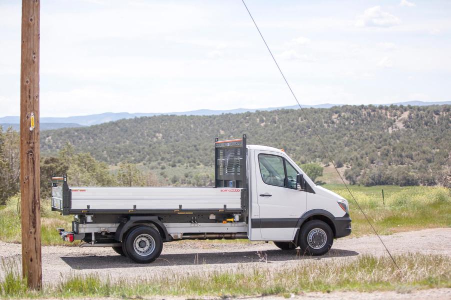 A shite Mercedes-Benz sprinter truck parked sideways on a dirt road, a ridge of mountains visible in the background.