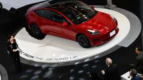 A red 2022 Tesla Model 3, one of the safest cars of 2022, parked on a white circle platform.