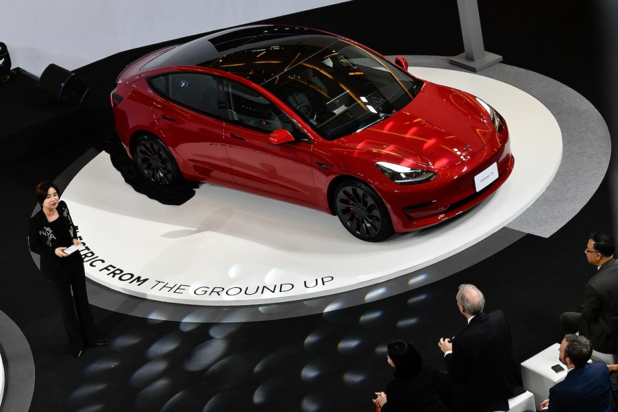 A red 2022 Tesla Model 3, one of the safest cars of 2022, parked on a white circle platform.