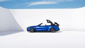 A BMW M4 Competition Convertible drops its sports car top against a white background.