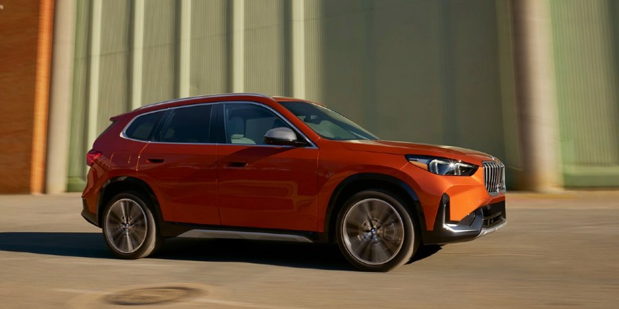 An orange 2023 BMW X1subcompact luxury SUV is driving.