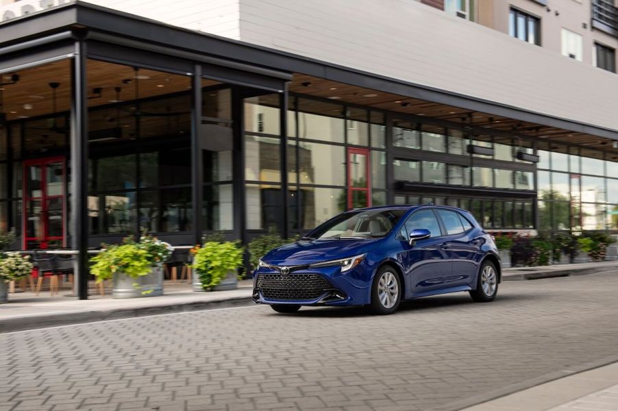 A blue 2023 Toyota Corolla Hatchback parks next to a business.