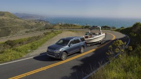 A new Ford Expedition tows a boat a tight corner with blue ocean in the background. The Expedition is an SUV alternative to Ford's pickup trucks.