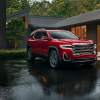 A red 2023 GMC Acadia parked outdoors after a rain in front of a house.