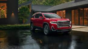 A red 2023 GMC Acadia parked outdoors after a rain in front of a house.