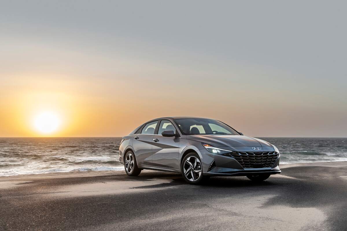 A grey 2023 Hyundai Elantra parked in front of a sunset on a beach, one of the best small cars of 2023.