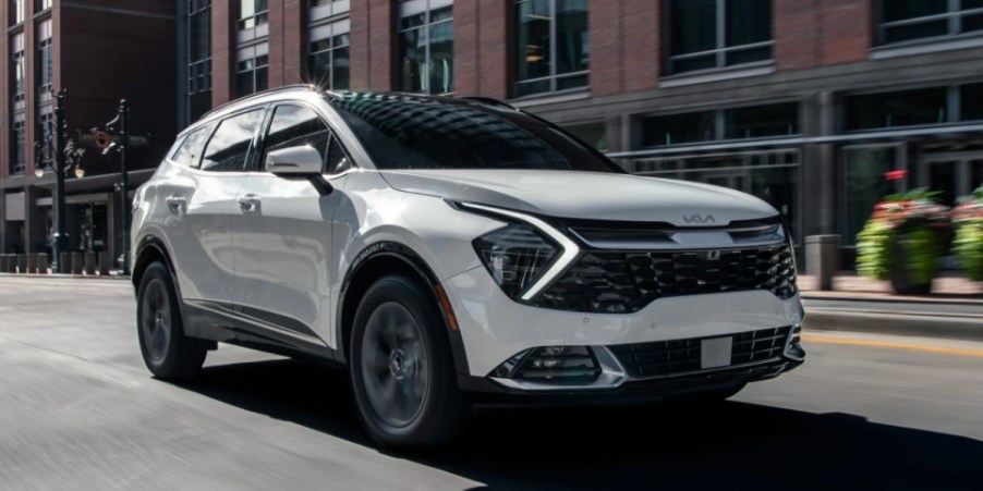 A white 2023 Kia Sportage Hybrid small hybrid SUV is driving on the road.