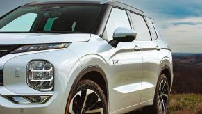 A white 2023 Mitsubishi Outlander PHEV compact crossover SUV model parked on a grassy hill.