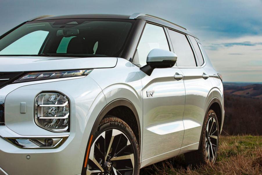 A white 2023 Mitsubishi Outlander PHEV compact crossover SUV model parked on a grassy hill.