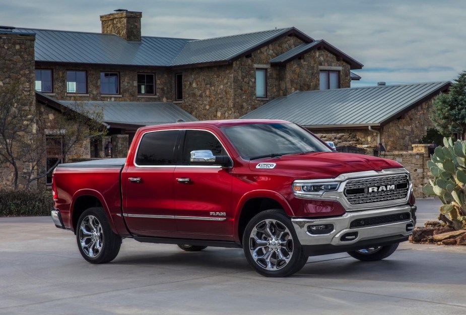 Red 5th gen Ram 1500 pickup truck parked in front of a stone house.