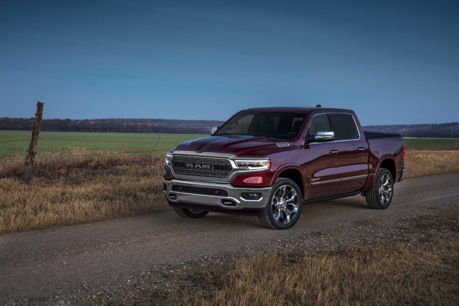 A red 2023 Ram 1500 half-ton pickup truck parked on a dirt road, a fence and field visible in the background.