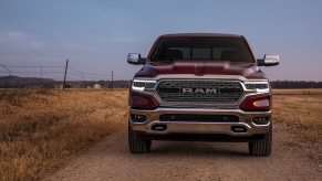 The grille of a red Ram 1500 pickup truck that could last for over 200k miles, a farm field visible in the background.