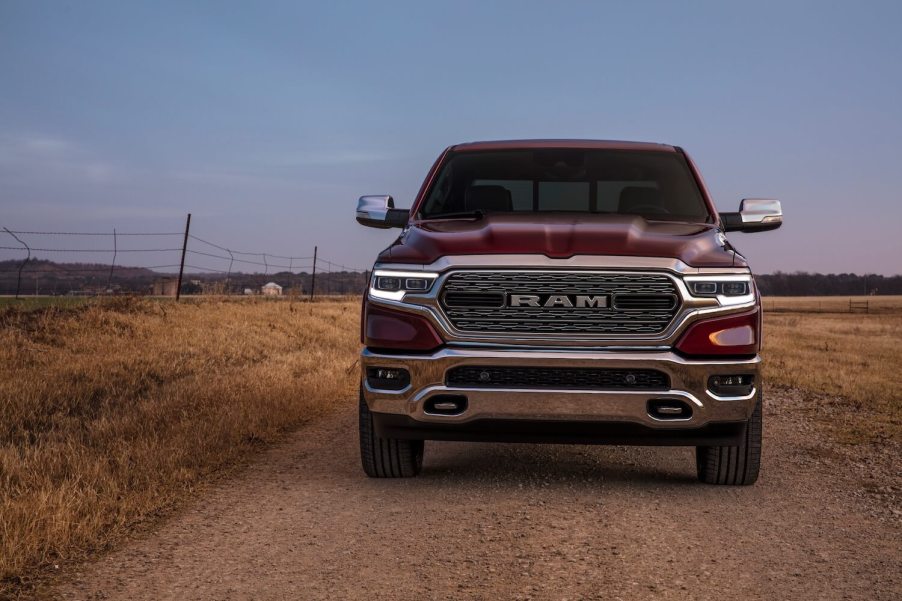 The grille of a red Ram 1500 pickup truck that could last for over 200k miles, a farm field visible in the background.