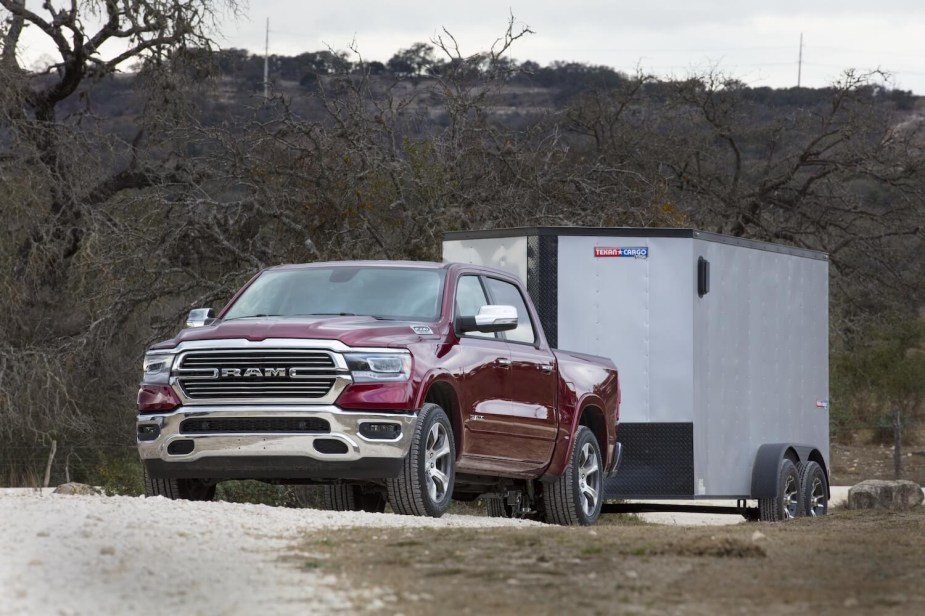 A red Ram 1500 pickup truck towing a covered trailer, trees and a mountain ridge visible in the background.