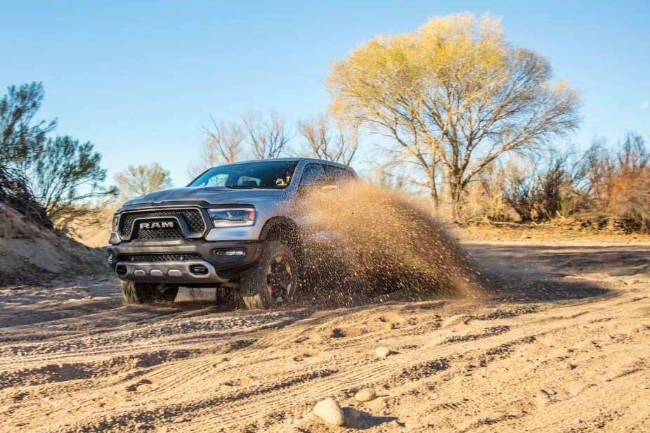 A silver Ram 1500 Rebel half-ton 4WD truck driving through sand, trees visible in the background.