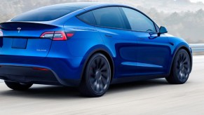 A blue 2023 Tesla Model Y small electric SUV is driving on the road.