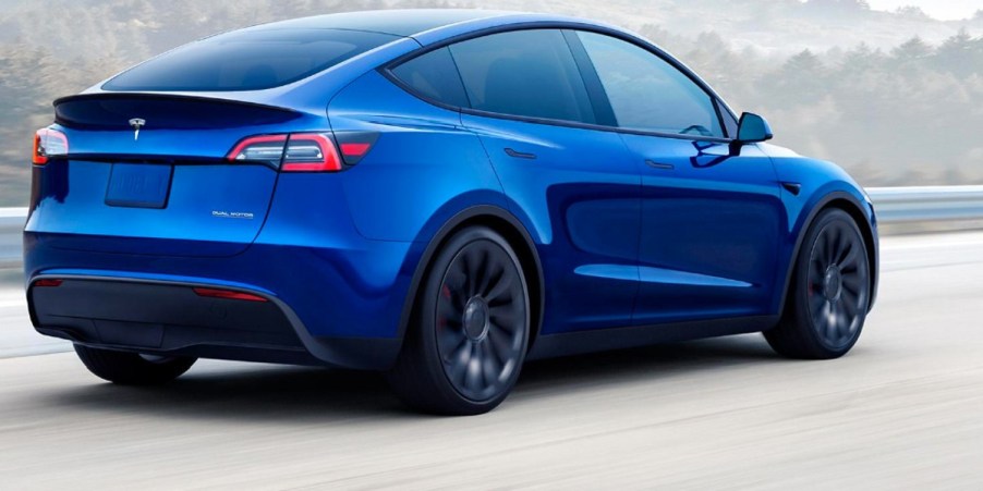 A blue 2023 Tesla Model Y small electric SUV is driving on the road.