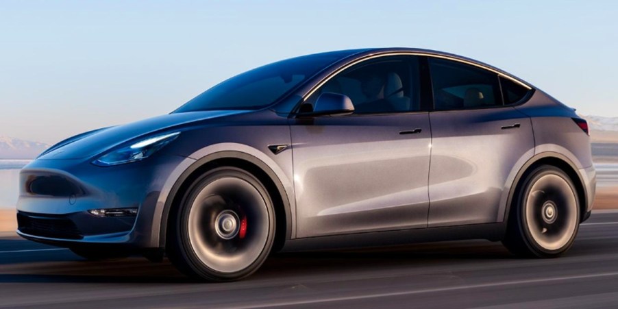 A gray 2023 Tesla Model Y small electric SUV is driving on the road.