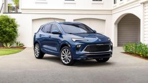 A blue 2024 Buick Encore GX Avenir subcompact crossover SUV parked on a driveway in front of a white luxury home