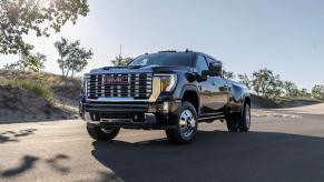 A black 2024 GMC Sierra 3500 HD heavy-duty pickup truck model parked in the middle of a road near sand dunes