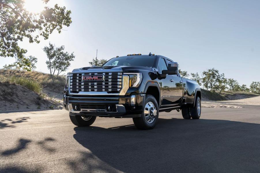 A black 2024 GMC Sierra 3500 HD heavy-duty pickup truck model parked in the middle of a road near sand dunes