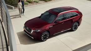 A red 2024 Mazda CX-90 parked outdoors with two people walking toward the car.