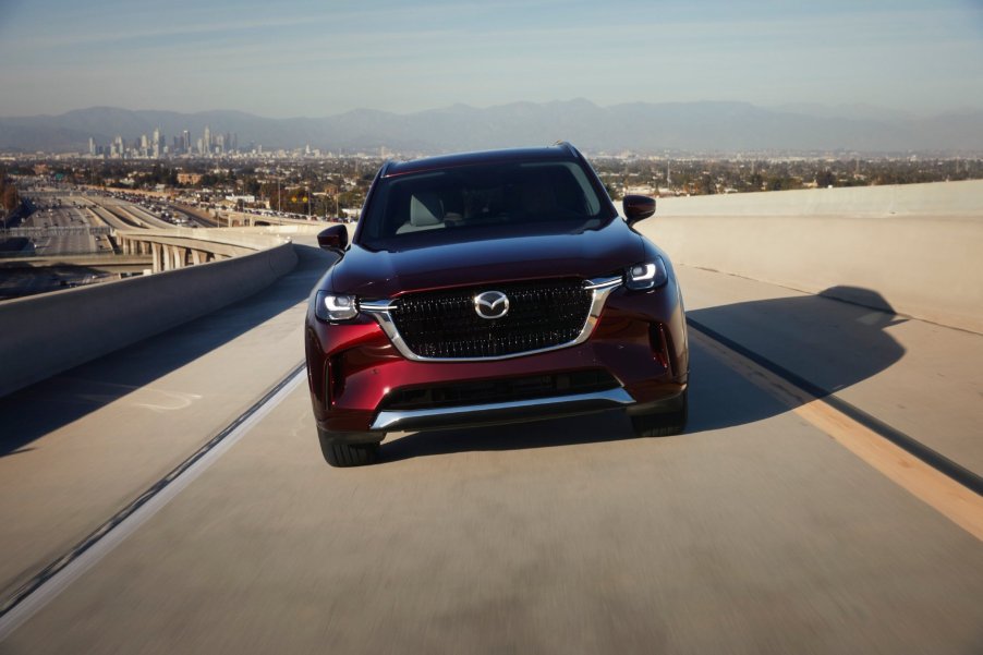 Front view of a new Mazda CX-90 in red driving down a highway with a straight-six engine under the hood.