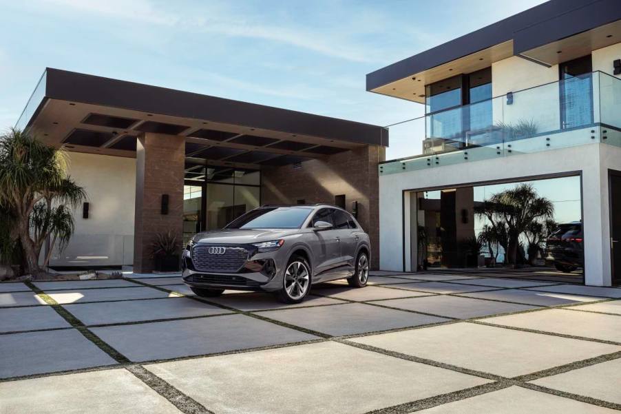 A grey Audi E-Tron electric SUV sits in front of a luxury home.