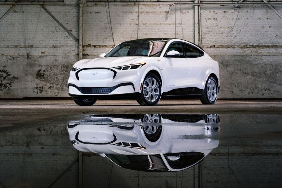 A white Mustang Mach-E and its mirror reflection off of a wet warehouse floor.