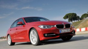 A used red 2014 BMW 328i cruises a coastal road.