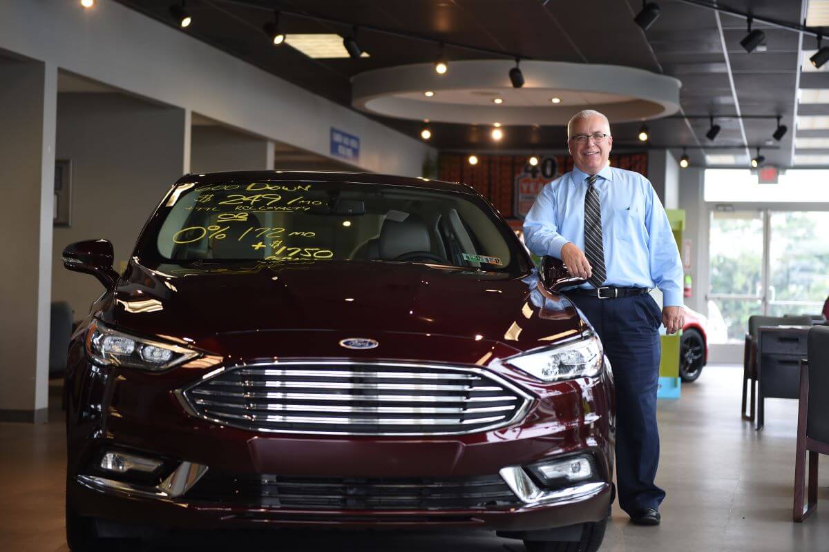 The Manderbach Ford general sales manager posing with a dark red Ford Fusion Energi hybrid midsize sedan model