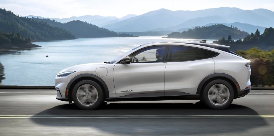 A white 2023 Ford Mustang Mach-E small electric SUV is driving on the road. 