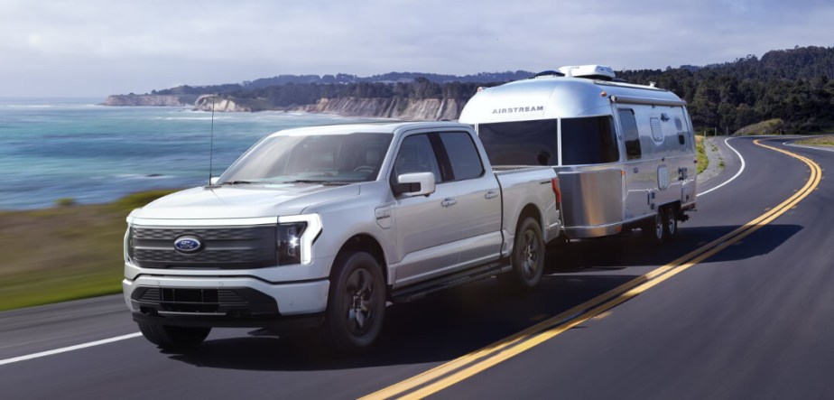 A Ford F-150 Lightning tows a trailer behind it as an electric truck.