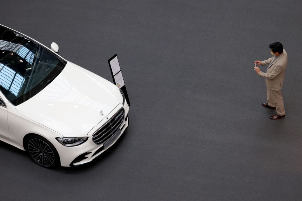 A man takes a picture of a Mercedes C-Class luxury car at an auto show.