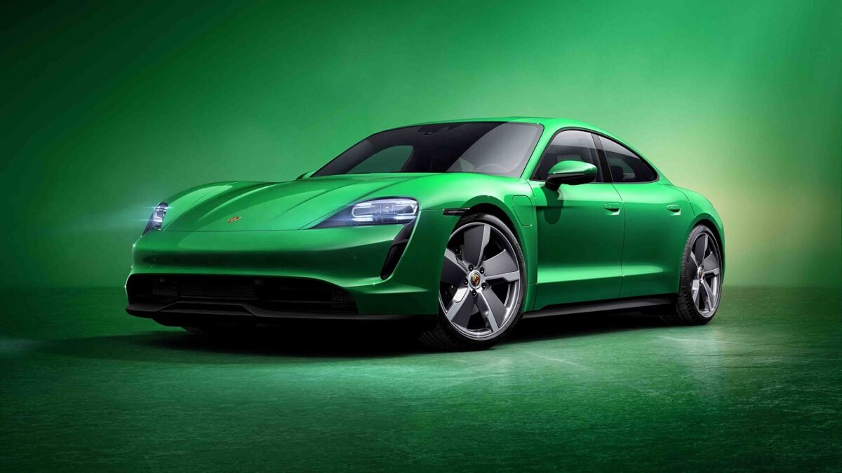 A bright green Porsche Taycan EV poses on a stage against a green background.