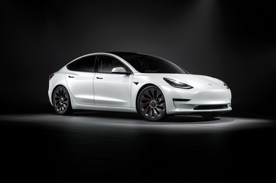 A white Tesla Model 3 EV parks under an overhead light.