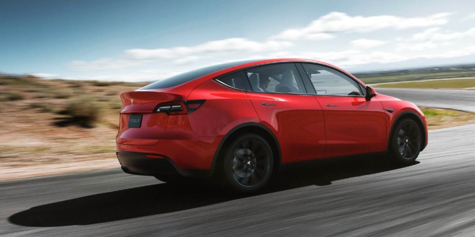 A red 2023 Tesla Model Y small electric SUV is driving on the road. 