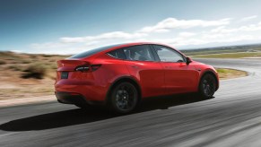 A red 2023 Tesla Model Y small electric SUV is driving on the road.