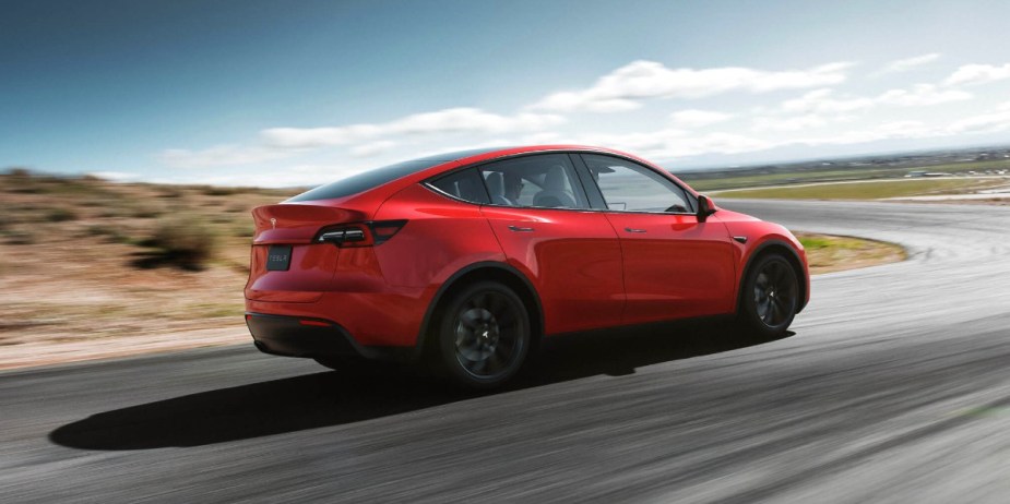 An orange 2023 Tesla Model Y small electric SUV is driving on the road. 