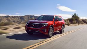 A red 2024 Volkswagen Atlas drives down a road with mountains in the background.