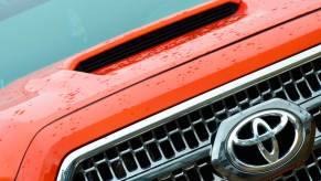 Closeup of the Toyota logo in the grille of an orange Tacoma pickup truck.