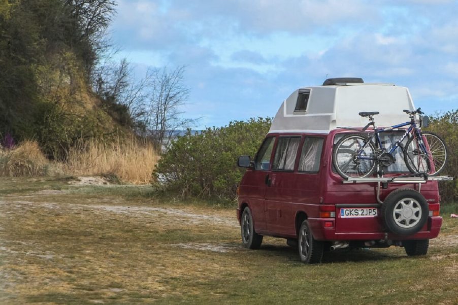 A maroon Volkswagen van parks in a camper site as travel junkies enjoy van life.