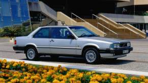 A 1985 Volvo 780 executive car model from the 700 Series parked in front of a row of yellow flowers