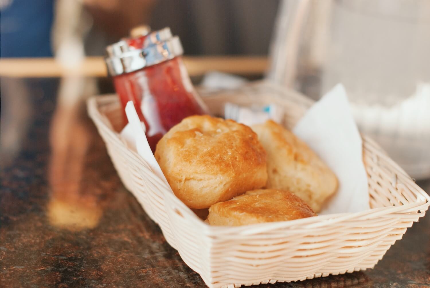 Three biscuits in a basket on a table, jam visible in the background.